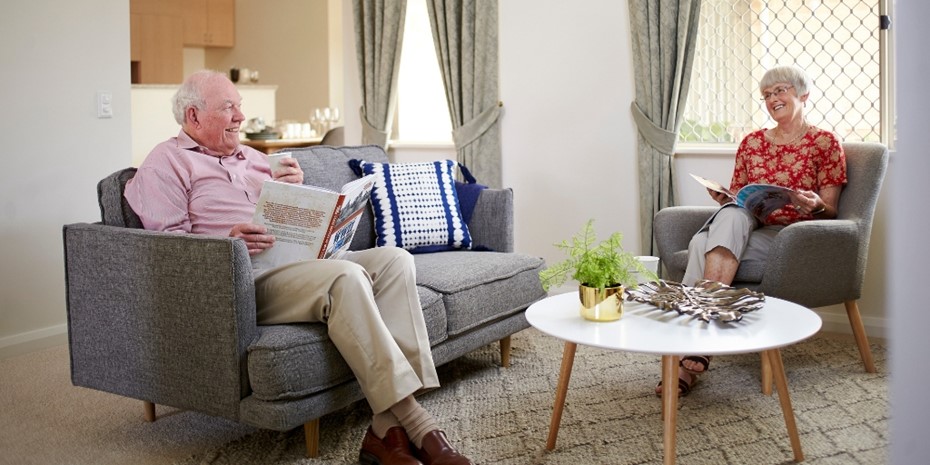 Elderly man in light pink shirt smiling and holding a book with his partner wearing a red shirt