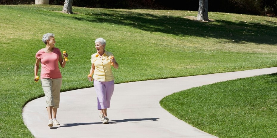 Two elderly women walking and smiling holding small weights