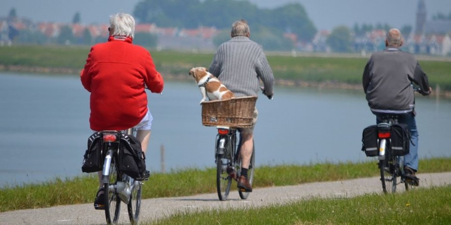 Three elderly people riding pushbiks along a river